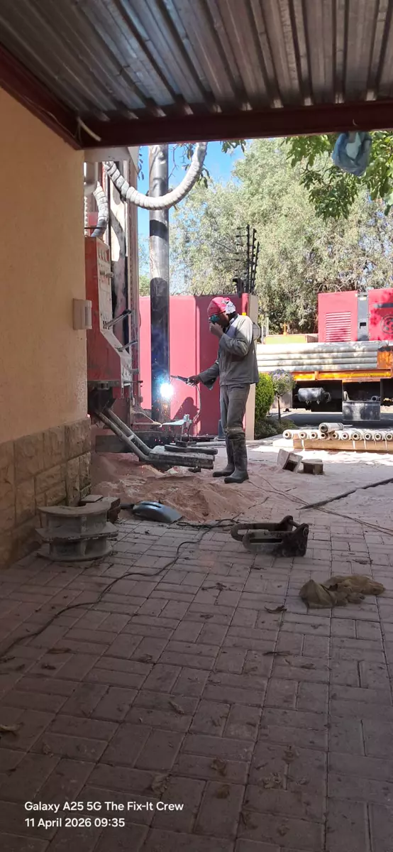 Worker welding outdoors next to industrial equipment