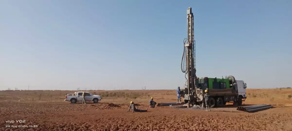Drilling rig truck and workers on a red earth field