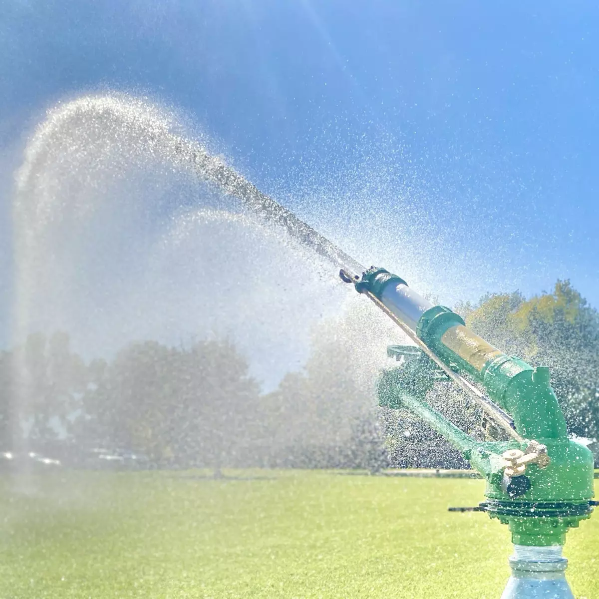 Green agricultural sprinkler spraying across a field