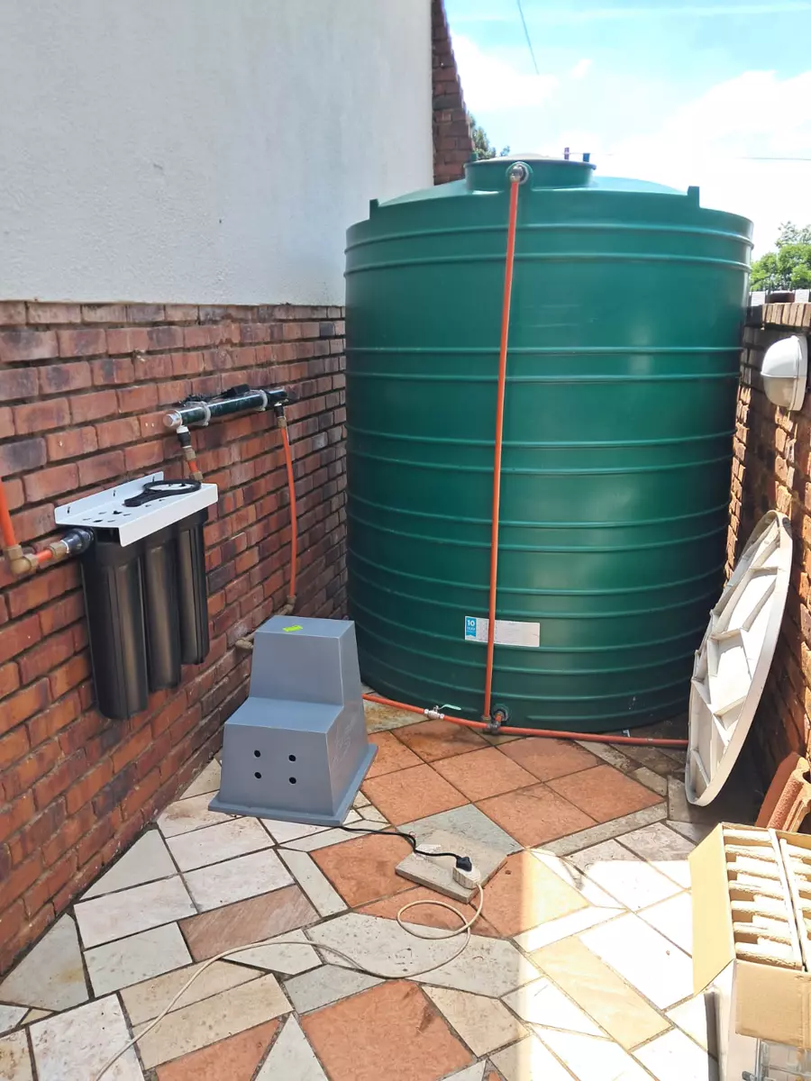 Large green water storage tank and filtration system against a brick wall