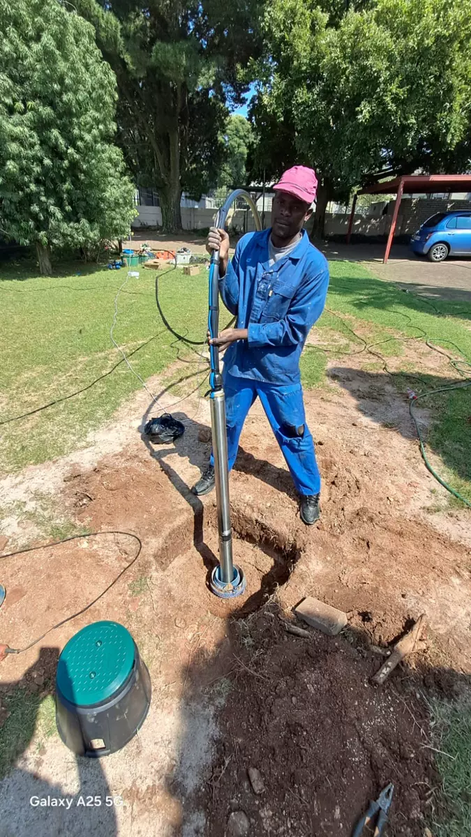 Worker in blue overalls installing a borehole pump