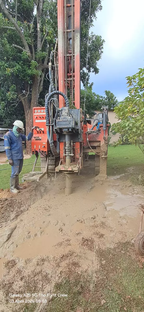 Orange drilling rig operating in terrain with a worker
