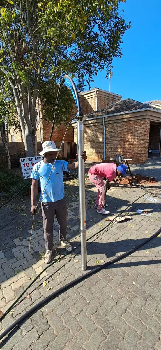 Two workers installing a borehole pump outdoors