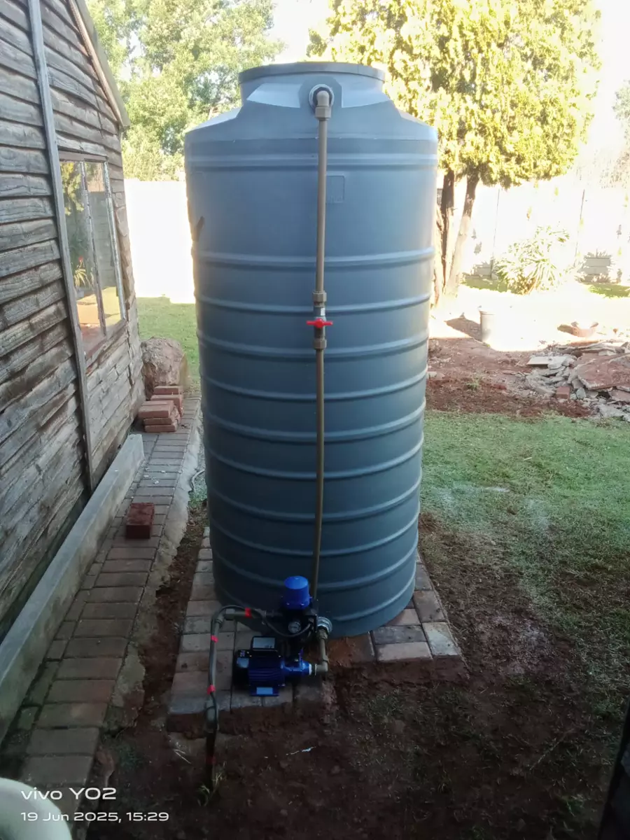 Grey water tank and pump installed next to a wooden shed